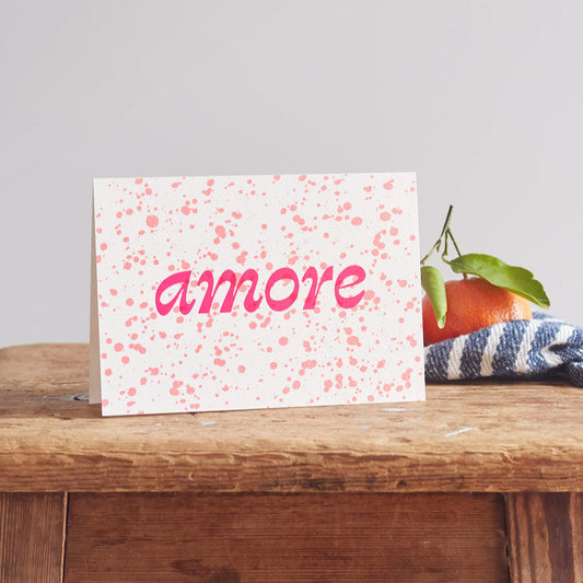 Card with 'amore' text on a wooden surface with an orange and leaves.